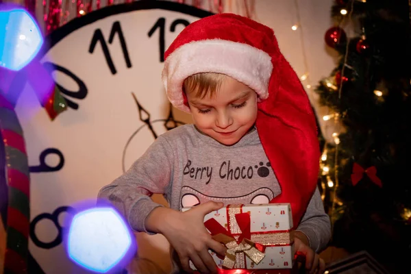 A child in a santa hat opens a gift — Stock Photo, Image