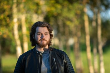 Renkli sonbahar yapraklarının bulanık arka planına bakan düşünceli, genç sakallı bir adam.