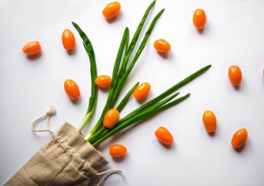 Turuncu renkli kiraz domatesleri bembeyaz arka planda maydanoz yeşillikleri ile bezenmiş.
