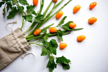 Turuncu renkli kiraz domatesleri bembeyaz arka planda maydanoz yeşillikleri ile bezenmiş.