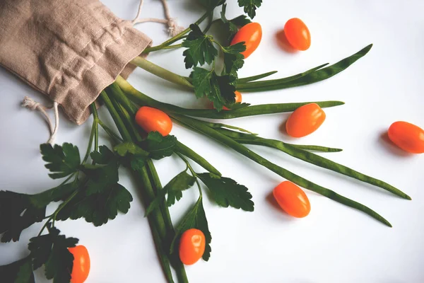 Turuncu renkli kiraz domatesleri bembeyaz arka planda maydanoz yeşillikleri ile bezenmiş.