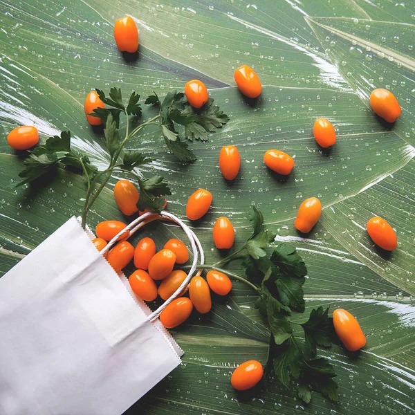 Yeşil yapraklı beyaz kağıt torba içinde yeşil turuncu domatesler.
