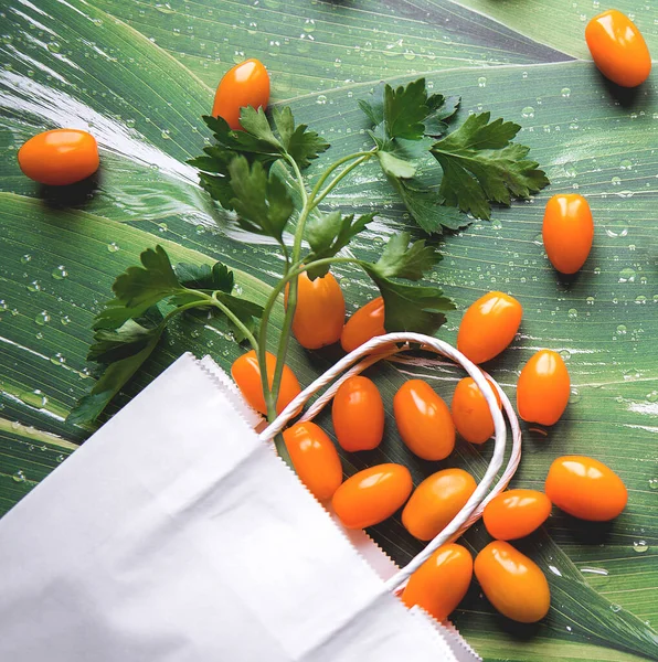 Yeşil yapraklı beyaz kağıt torba içinde yeşil turuncu domatesler.