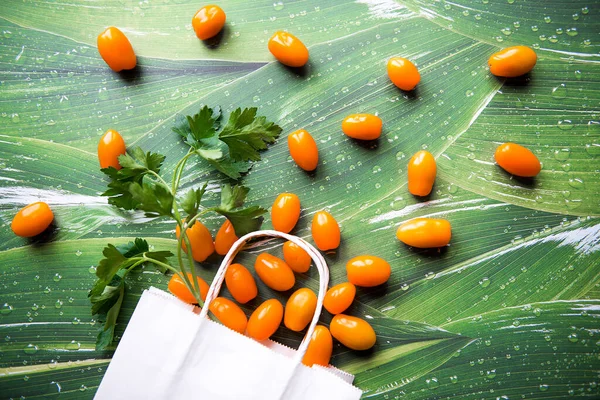 Yeşil yapraklı beyaz kağıt torba içinde yeşil turuncu domatesler.