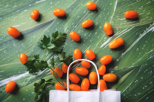 Yeşil yapraklı beyaz kağıt torba içinde yeşil turuncu domatesler.