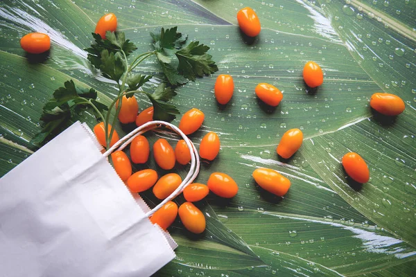 Yeşil yapraklı beyaz kağıt torba içinde yeşil turuncu domatesler.