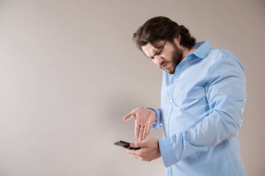 Gri arka planda cep telefonuna bağıran mavi gömlekli agresif genç iş adamı.