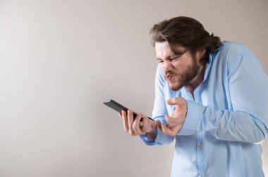 Gri arka planda cep telefonuna bağıran mavi gömlekli agresif genç iş adamı.
