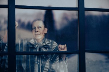 Thoughtful middle-aged woman looks through a dirty window glass