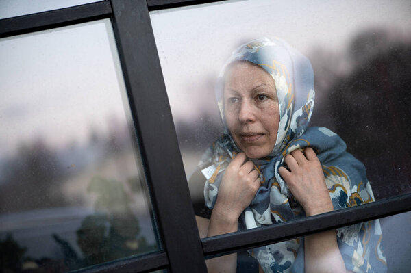 Smiling middle-aged woman with scarf on head looking through dirty window glass