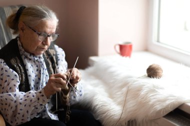 Pencere kenarında örgü ören yaşlı bir kadın.