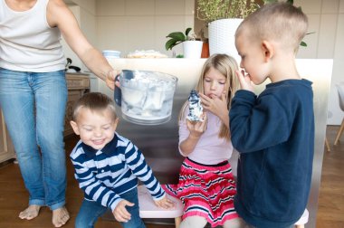 Anne ve üç çocuk mutfakta yemek pişiriyor.
