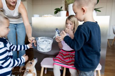 Anne ve üç çocuk mutfakta yemek pişiriyor.