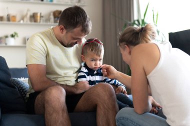 Anne ve baba ağlayan bir bebeği teselli eder, anne gözyaşlarını siler.