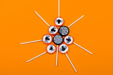 Siyah örümcekli Cadılar Bayramı şekeri ve turuncu arka planda örümcek ağı, üst görünüm