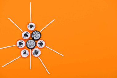 Siyah örümcekli Cadılar Bayramı şekeri ve turuncu arka planda örümcek ağı, üst görünüm