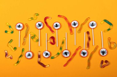 Siyah örümcekli Cadılar Bayramı şekeri, örümcek ağı ve turuncu arka planda lezzetli jöle solucanları.