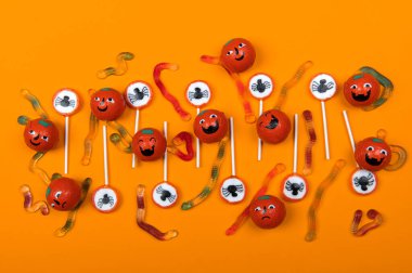 Siyah örümcekli Cadılar Bayramı şekeri, örümcek ağı, gülümseyen balkabakları ve turuncu arka planda jöle solucanları.