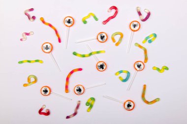 Beyaz arka planda siyah örümcekler ve jöle solucanları olan renkli Cadılar Bayramı şekerleri.