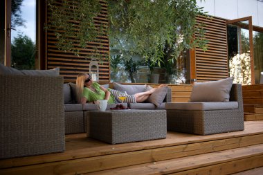 Hoş, orta yaşlı, mutlu bir kadın yaz terasında dinleniyor. Taze meyve suyu kokteyli içiyor ve olumlu duygular besliyor.