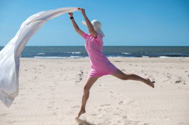 happy woman with a blanket flies over a sandy beach by the sea on a sunny summer day 