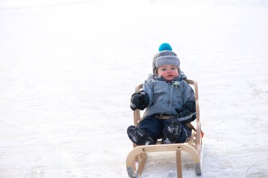 Küçük çocuk kızakta oturuyor. Kış günü kızağında oturan tatlı küçük çocuk. Kış oyunu, kar, kızak - güzel çocuk karda eğleniyor. Küçük çocuk kızakla gezintiye çıkıyor. Eğlenceli bir aile. 