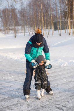 Küçük oğluna buz pateni pistinde buz pateni öğreten genç bir anne. Aile buz pateni sahasında kışın keyfini çıkarır.