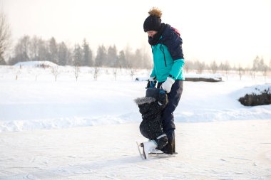 Genç bir anne, oğluna buz pateni pistinde buz pateni öğretiyor. Aile buz pateni sahasında kışın keyfini çıkarır.