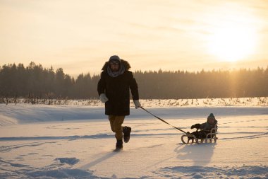 Baba, kışın açık havada kızakla gezerken çocuğu çekiyor. Güzel akşam güneşi.