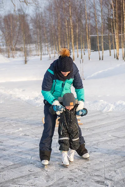 Küçük oğluna buz pateni pistinde buz pateni öğreten genç bir anne. Aile buz pateni sahasında kışın keyfini çıkarır.