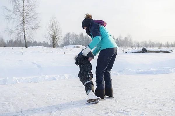 Küçük oğluna buz pateni pistinde buz pateni öğreten genç bir anne. Aile buz pateni sahasında kışın keyfini çıkarır.