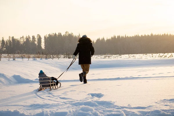 Baba, kızakla çocuğu çekiyor. Soğuk kış gününde açık havada yürüyor.. 