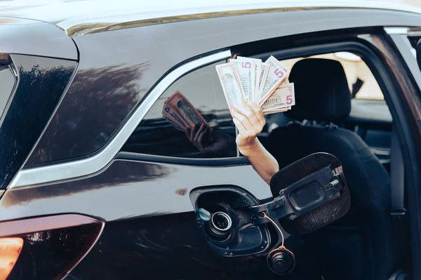 woman hand hold cash dollar bills next to car with an open tank, concept of rising fuel prices