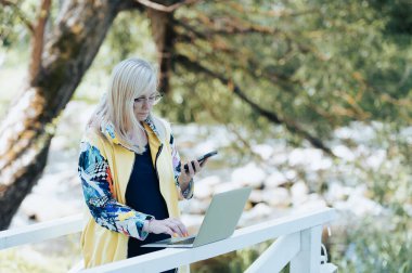 Laptop ve cep telefonuyla şehir parkında uzaktan iletişim kuran meşgul bir iş kadını.