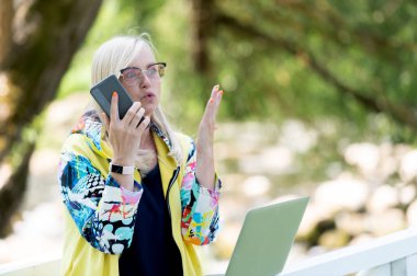 Şehir parkında bilgisayarlı ve cep telefonlu kızgın bir iş kadını.