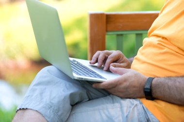 Parkta otururken dizüstü bilgisayarda çalışan ve daktilo kullanan bir adam.