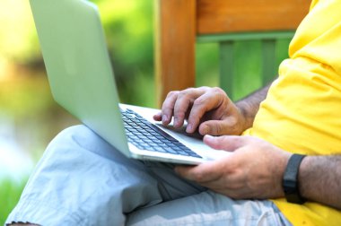 Parkta otururken dizüstü bilgisayarda çalışan ve daktilo kullanan bir adam.