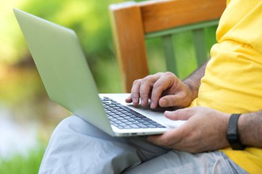 Parkta otururken dizüstü bilgisayarda çalışan ve daktilo kullanan bir adam.