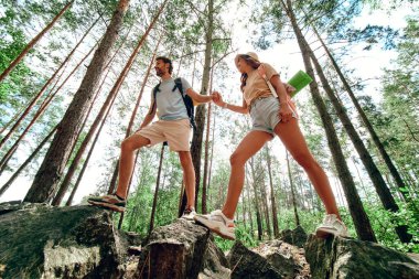 Sırt çantalı iki turist ormandaki kayalık tepelere tırmanıyor. Kamp, seyahat, yürüyüş..