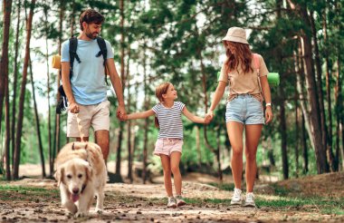 Sırt çantalı ve labrador köpeği olan mutlu bir aile ormanda yürüyor. Kamp, seyahat, yürüyüş..