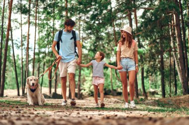 Sırt çantalı ve labrador köpeği olan mutlu bir aile ormanda yürüyor. Anne baba ve kızları hafta sonu. Kamp, seyahat, yürüyüş..