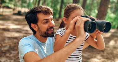 Genç baba küçük kızına çam ormanında dürbünle bakmayı öğretiyor. Kamp, dinlenme, yürüyüş..