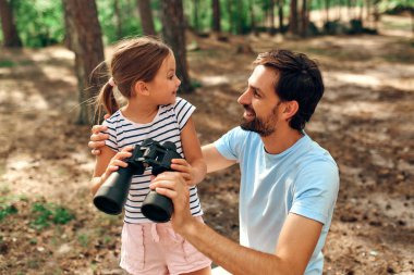 Genç baba küçük kızına çam ormanında dürbünle bakmayı öğretiyor. Kamp, dinlenme, yürüyüş..