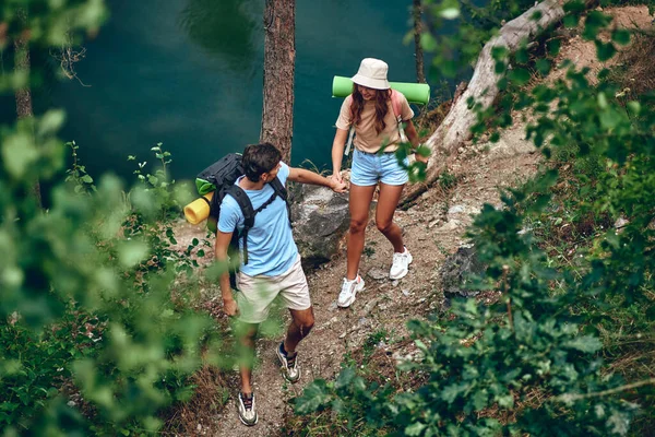 バックパック付きのハイキングを楽しむカップルが川沿いの森を歩きます キャンプ旅行ハイキング — ストック写真