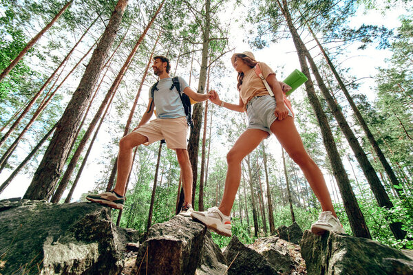 A loving couple of tourists with backpacks climb the rocky peaks in the forest. Camping, travel, hiking.