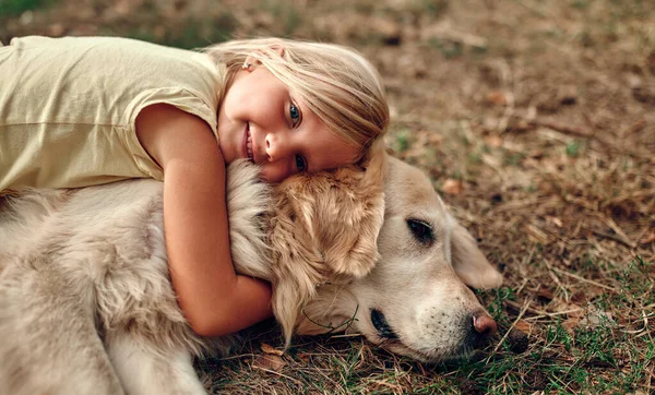 Słodka Blondynka Dziewczynka Leży Trawie Przytulając Swojego Przyjaciela Psa Labrador — Zdjęcie stockowe