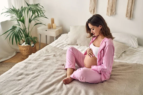 年轻的孕妇坐在卧室的床上 双手轻轻地放在肚子上 产妇概念 — 图库照片