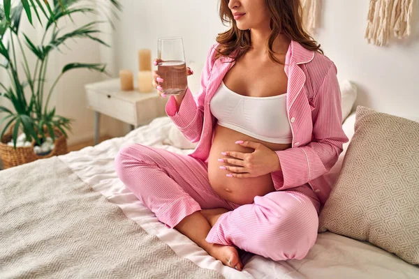 年轻的孕妇坐在卧室的床上 喝着一杯水 水平衡 产妇概念 — 图库照片
