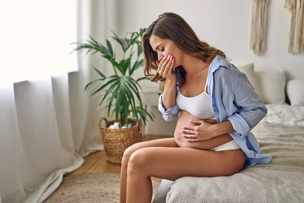 Mujer Embarazada Joven Enfermó Sentada Cama Dormitorio Sosteniendo Estómago Tosiendo —  Fotos de Stock