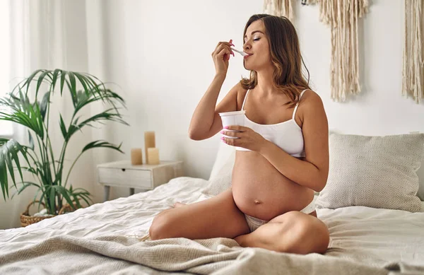 Молодая Беременная Женщина Белых Трусах Сидит Кровати Спальне Ест Йогурт — стоковое фото